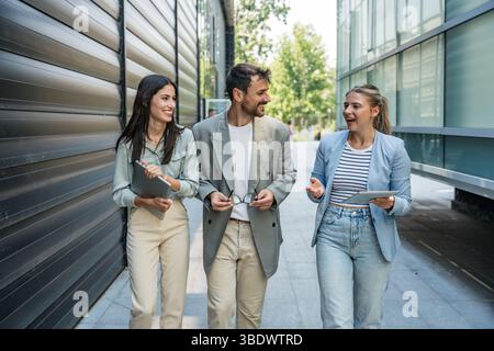 Diverse business team of corporate professionals in formal attire collaborating outdoors, engaged in strategic discussion while analyzing data on lapt Stock Photo