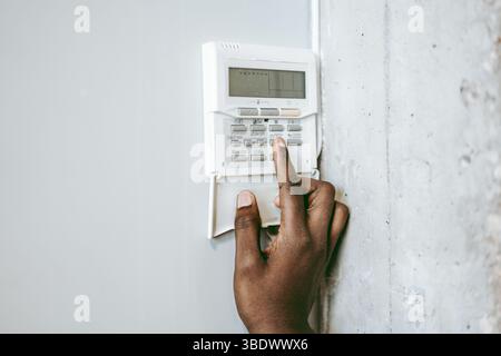 Person interacting with a security panel on a wall in a modern setting during daytime Stock Photo