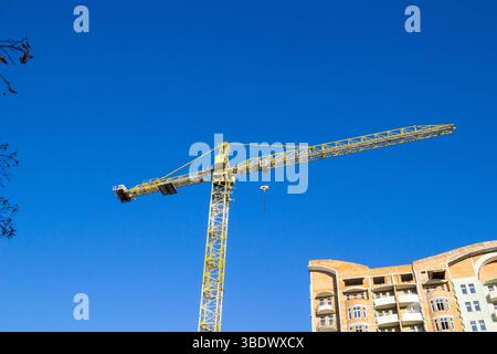 A construction crane and a part of an unfinished house made of ceramic bricks against a blue sky. Stock Photo