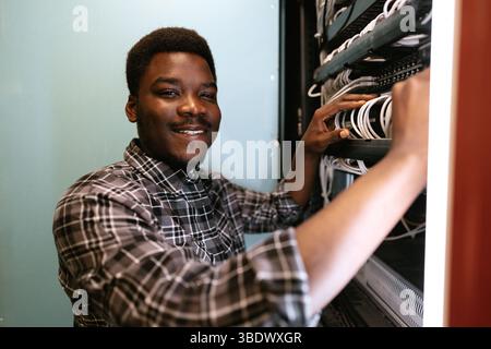 Technician organizes network cables in server room during daytime, ensuring efficient connectivity Stock Photo