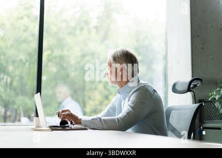 Mature 40s focused businessman, executive director working using laptop, doing data base online research sitting at office. Successful business man, l Stock Photo