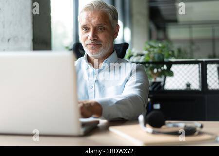Mature 40s focused businessman, executive director working using laptop, doing data base online research sitting at office. Successful business man, l Stock Photo