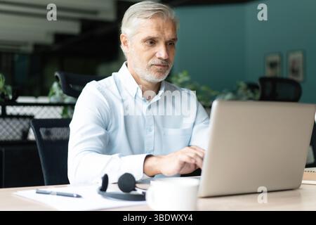 Mature 40s focused businessman, executive director working using laptop, doing data base online research sitting at office. Successful business man, l Stock Photo