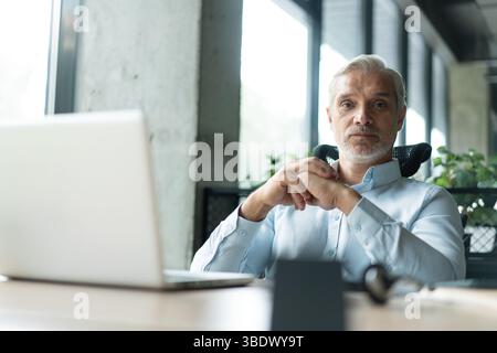Happy mature professional business man looking at camera sitting at work desk using computer. Portrait of smiling male company worker employee, projec Stock Photo