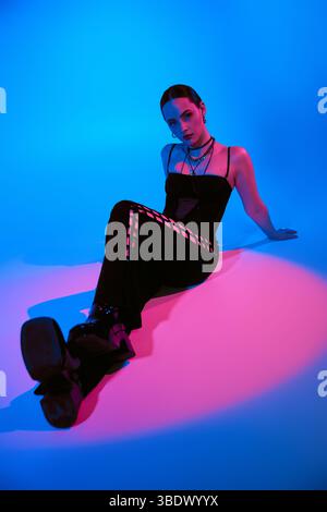 Stylish young woman poses confidently in a chic outfit, illuminated by colorful lighting. Stock Photo