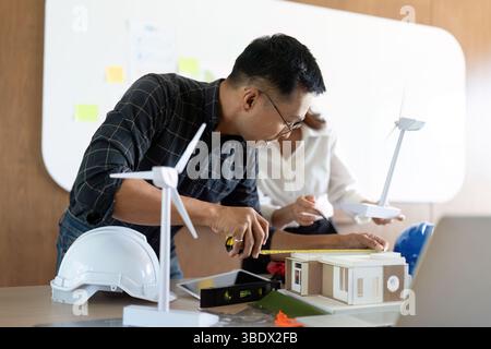 Sustainability and Engineering. Engineers collaborating on eco-friendly building design with wind turbines. Stock Photo