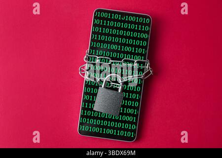 A smartphone with a screen displaying binary code, secured with a chain and a lock. A concept of internet and virtual security. Stock Photo