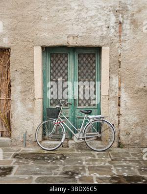 A vintage bicycle leaning against an old, weathered wooden door, on a stone wall. Evocative scene of daily life. Stock Photo