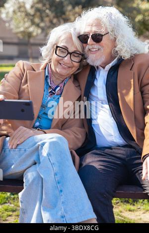 Senior couple taking selfie outdoors with smartphone, smiling and sunglasses Stock Photo
