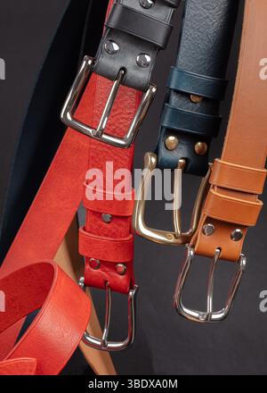 Various leather belts with metal buckles close-up on dark grey background. Stock Photo