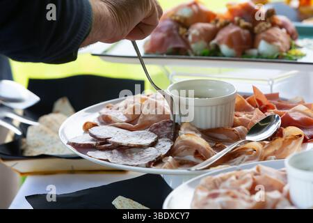 Chef serves a platter of assorted italian cured meats, including prosciutto, salami, and coppa, at an outdoor buffet Stock Photo