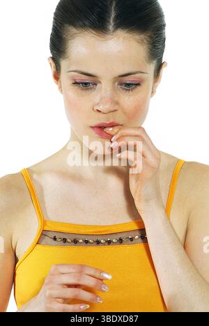 Close up of young woman wearing yellow tank top biting her nail. Portrait Stock Photo