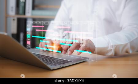 Businessman using project management software on a laptop to schedule tasks, update Gantt charts, and manage workflow, enhancing planning, productivit Stock Photo