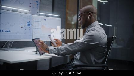 African American Financial Analyst Analyzing Real-Time Stocks, Exchange Market Charts on Digital Tablet, Smartphone and Computer with Multi-Monitor Workstation. Businessman in Investment Bank Office. Stock Photo
