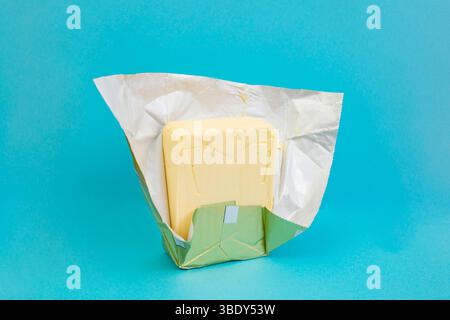 Yellow organic butter stick in a golden foil pack on blue background Stock Photo