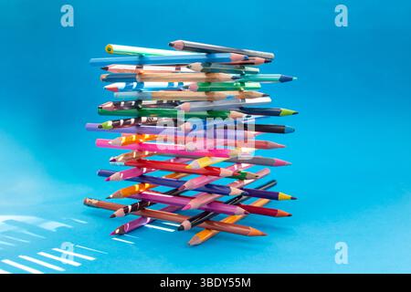 Stacked colored crayons stacked in the shape of a high tower illuminated with sun light on blue Stock Photo