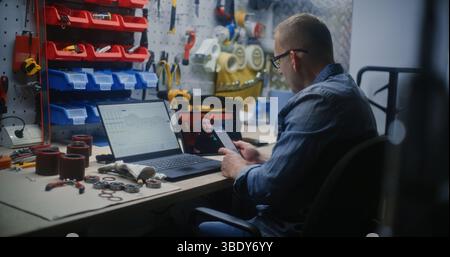 Handyman Checking Real-Time Stocks and Exchange Market Charts Using Laptop Computer and Phone, Watching Online Trading Tutorial on Digital Tablet. Man Studying Trading Remotely Working in Workshop. Stock Photo