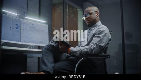 Financial Analyst Analyzing Real-Time Stocks, Exchange Market Charts Using Digital Tablet and Computer with Multi-Monitor Workstation. African American Businessman Works in Investment Bank Office. Stock Photo