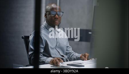African American Professional Financial Analyst or Stock Exchange Broker Typing on Keyboard, Using Computer. Successful Businessman Working in Investment Bank Office or Financial Agency at Night. Stock Photo