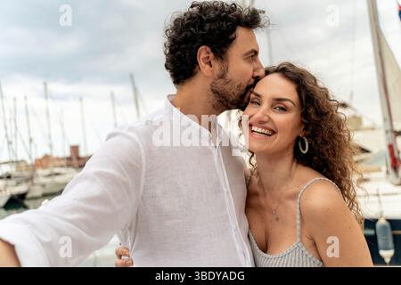 Smiling couple embracing and taking a selfie during summer holiday at the marina. Concept of love, travel, romantic moments and lifestyle by the sea. Stock Photo