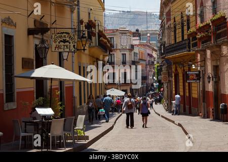 Guanajuato City, Mexico - May 30th 2016: People stroll down a cobblestone street lined with colorful buildings, hotels, and restaurants. Stock Photo