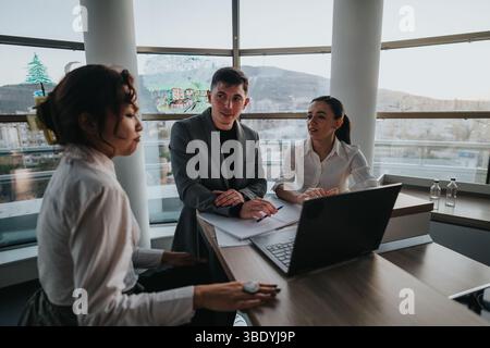 Three business professionals engaged in a focused conversation around a laptop in a contemporary office. Stock Photo