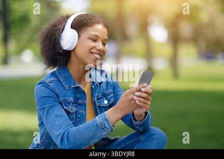 Smiling black female student listening music and browsing smartphone while relaxing outdoors Stock Photo