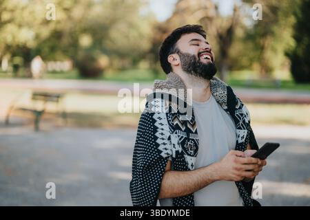 Man laughing while using smart phone outdoors in a sunny park Stock Photo