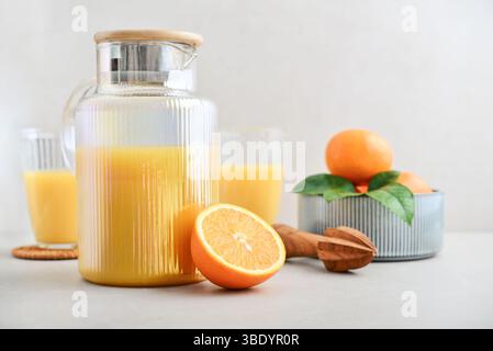 Orange fresh squeezed juice in glass and glasses jug with ripe oranges and olive wood squeezer on light background Stock Photo