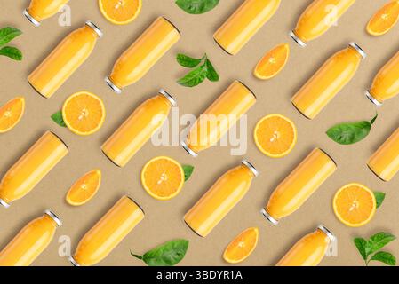 Pattern from bottles of orange juice and orange slices with leaves on craft paper background, top view Stock Photo