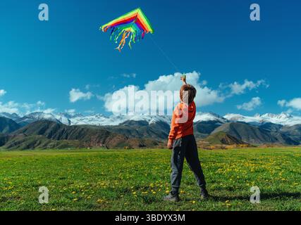 Happy boy with kite on green field on mountains background Stock Photo