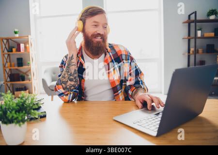 Bearded man wearing headphones works on a laptop at home while enjoying music and a casual indoor ambiance Stock Photo