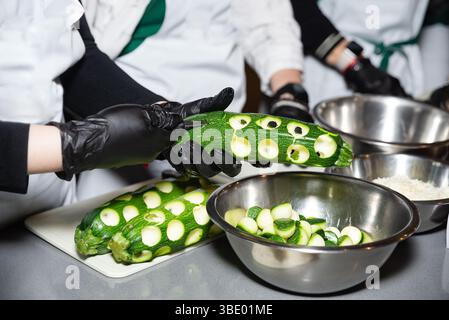 Close-up of chefs using a knife to carve circular slices from fresh zucchini during a professional cooking session. Stock Photo