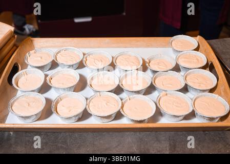 A tray filled with foil baking cups containing light brown cupcake or muffin batter, ready to be placed in the oven. Stock Photo