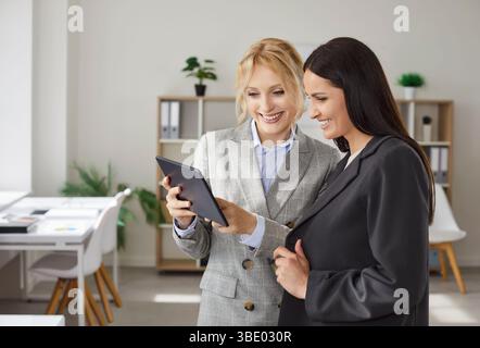 Two businesswomen collaborating together, focused in tablet, working on project Stock Photo