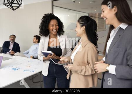 Three multiethnic professional businesswomen engaging in cheerful conversation Stock Photo