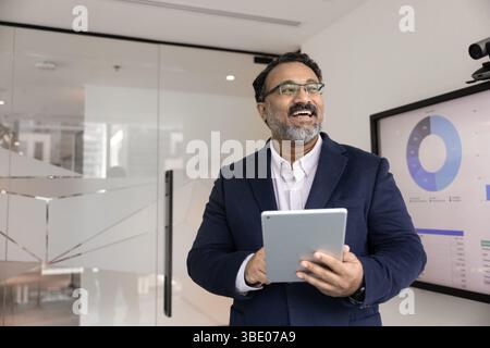 Smiling mature 45s Indian businessman holding tablet in workspace Stock Photo