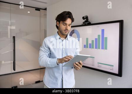 Focused Hispanic businessman working in office using tablet Stock Photo
