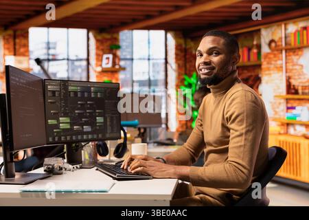 Portrait of cheerful IT technician using PC in innovative startup office and programming languages to build applications. Joyous software development agency IT expert optimizing code on computer Stock Photo