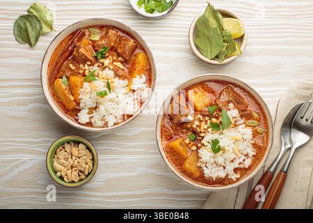 Two bowls of delicious massaman curry with beef, potatoes, rice, and peanuts, garnished with parsley on white wooden background, Thai cuisine Stock Photo