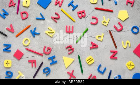 Colorful alphabet letters, numbers, forms, math signs, and crayons scattered on a concrete surface. Back to school concept. Stock Photo