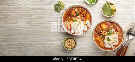 Two bowls of delicious massaman curry with beef, potatoes, rice, and peanuts, garnished with parsley on white wooden background, Thai cuisine Stock Photo