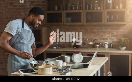 Black man baking pastry and using laptop in kitchen Stock Photo