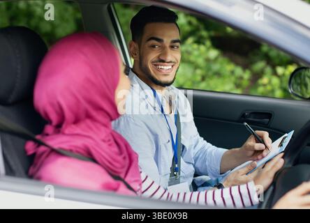 Driving School Test. Handsome Young Arab Instructor Examining Muslim Female Drive Stock Photo