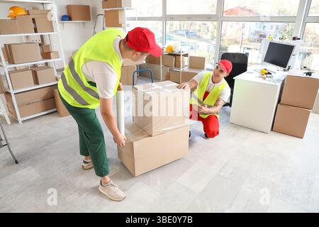 Male loaders wrapping boxes with stretch film in warehouse Stock Photo