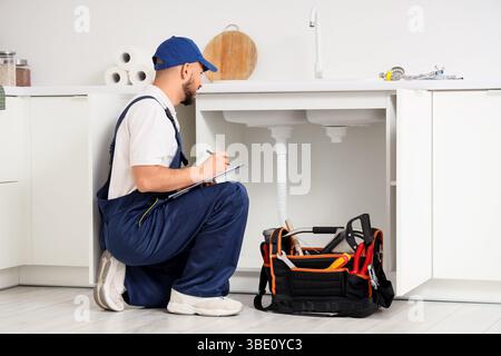 Male plumber with clipboard near sink in kitchen Stock Photo