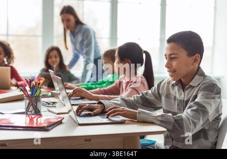 Cheerful Black Schoolboy Using Laptop Computer Learning Online In Classroom Stock Photo