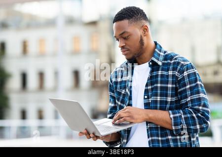 Black man using laptop, standing in city Stock Photo