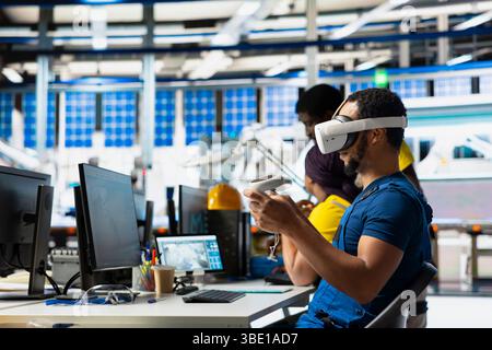 Photovoltaics facility specialist using VR tech to build models of alternative energy generators. Solar panels factory male employee building safe solar cells using virtual reality gear. Stock Photo