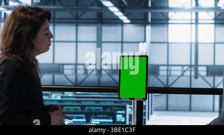 Programmers in data center brainstorming, using mockup tablet, observing equipment analytics. Server hub IT coworkers use isolated screen device, adjusting system parameters, camera A Stock Photo